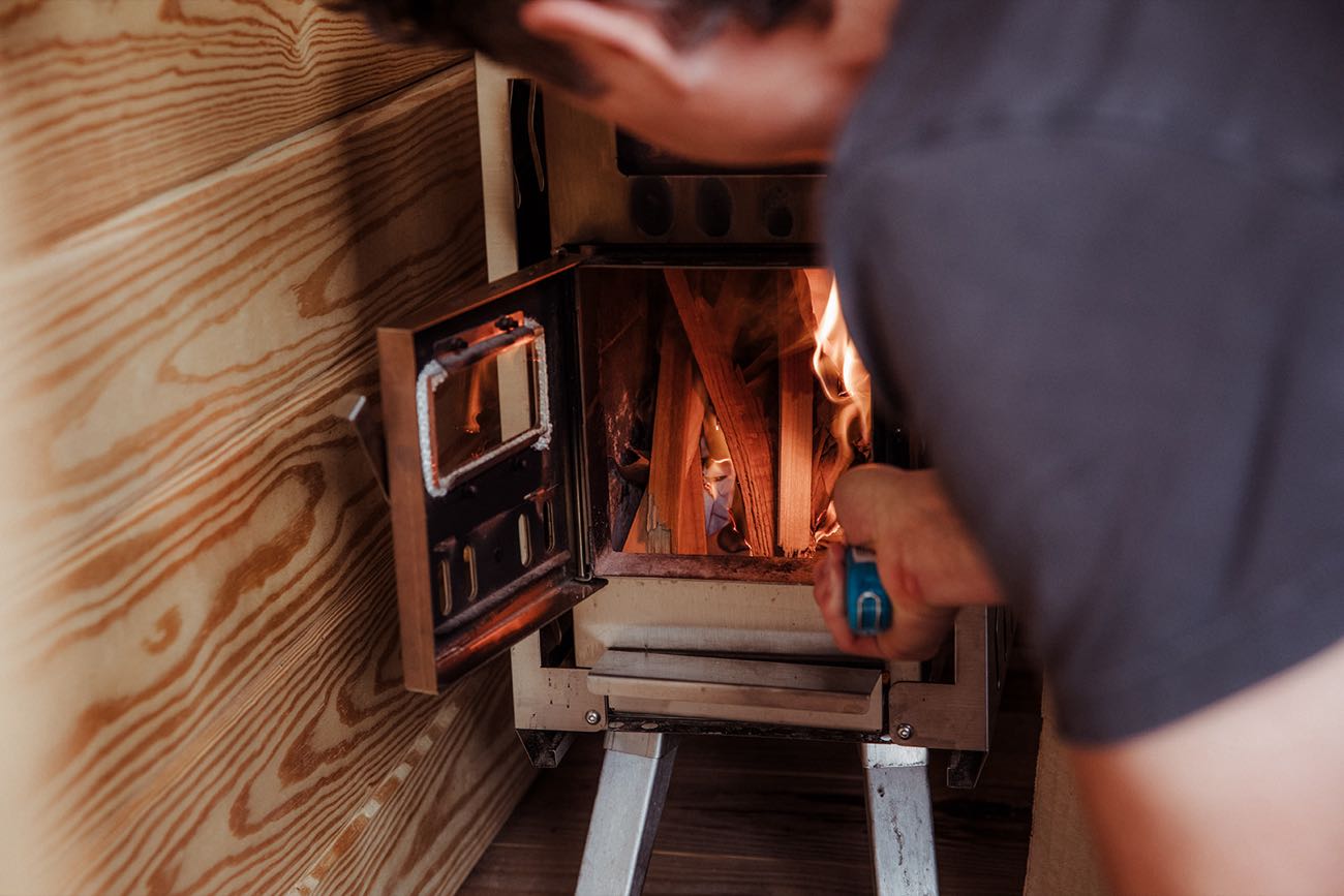 Hands lighting kindling in the sauna stove against the pine wall of the interior