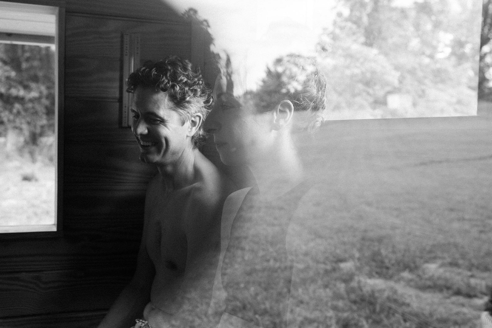 A soft double-exposure portrait of two people resting outside the sauna after a round, the field showing through the frame