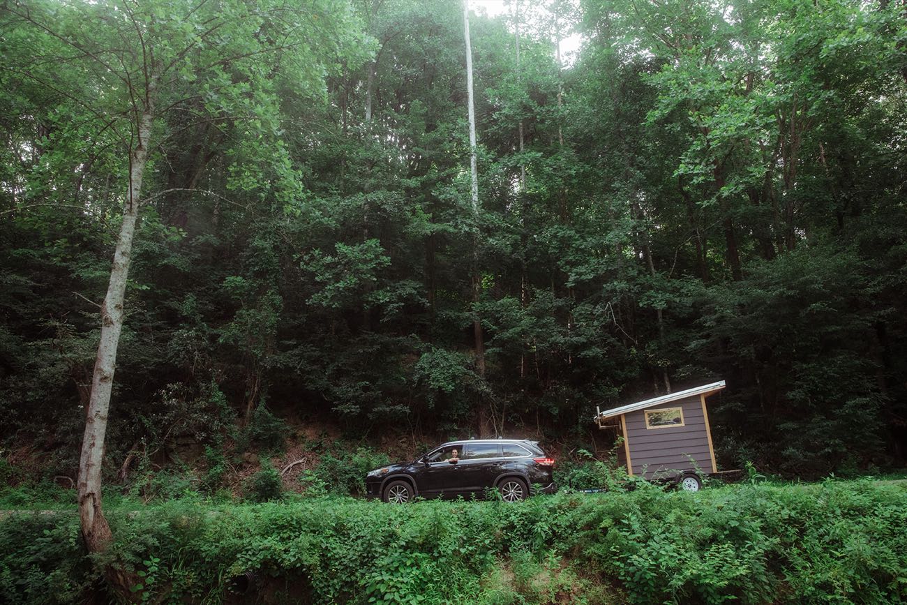 The sauna towed behind an SUV on a narrow road cut into the hillside, dense green canopy closing overhead